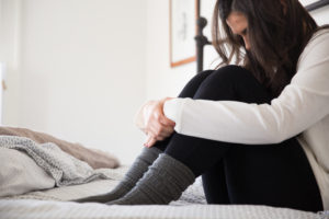 Anxious and depressed woman sitting on her bed, holding her knees.
